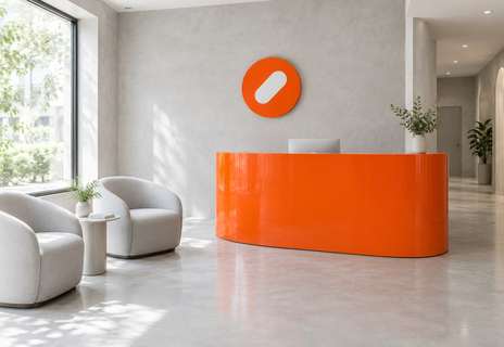 The Pulse Clinic reception with a curved orange desk, white armchairs and a round orange sign