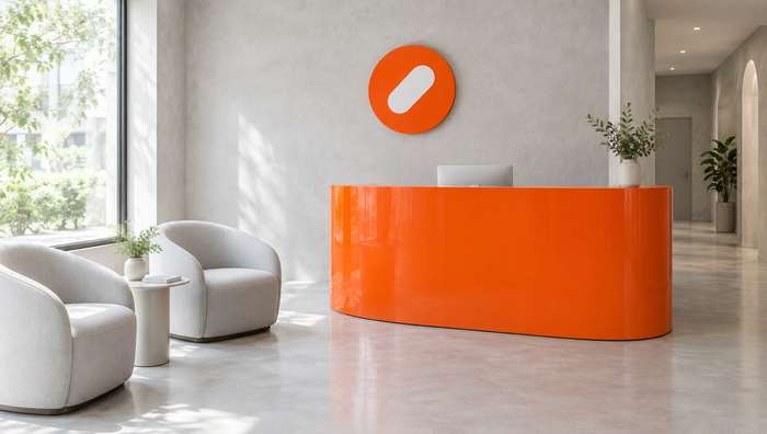 The Pulse Clinic reception with a curved orange desk, white armchairs and a round orange sign