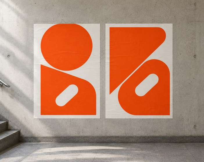 Two orange and white Nord Rail posters with bold shapes on a concrete wall