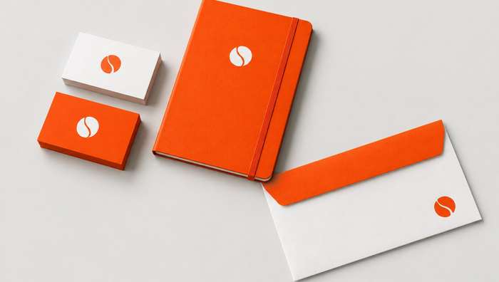 Halden Studio stationery: an orange notebook, orange and white business cards and an envelope